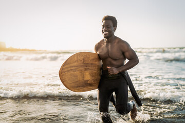 Male afro surfer having fun surfing during sunset time - African man enjoying surf day - Extreme sport lifestyle people concept