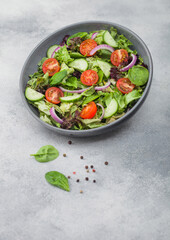 Grey bowl in motion with healthy fresh vegetables salad with lettuce and tomatoes, red onion and spinach on light background.