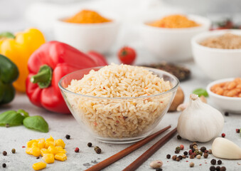 Glass bowl plate with boiled red long grain basmati rice with vegetables on light table background with sticks and paprika pepper with corn,garlic and basil. Top view