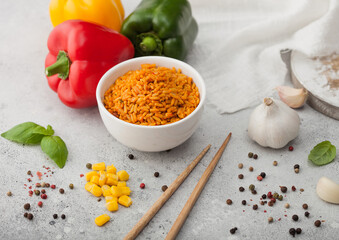 White ceramic bowl plate with boiled red long grain basmati rice with vegetables on light table background with sticks and paprika pepper with corn,garlic and basil. Top view