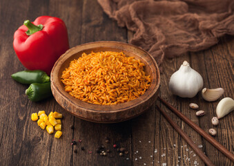 Wooden bowl with boiled red long grain basmati rice with vegetables on wooden table background with sticks and red paprika with corn,garlic and basil.