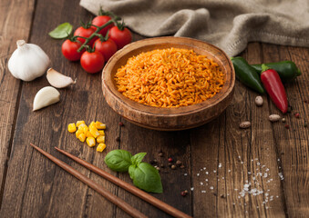 Wooden bowl with boiled red long grain basmati rice with vegetables on wooden table background with sticks and tomatoes with corn,garlic and basil. Top view