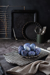 Easter eggs painted with natural blueberry dye lie on a plate against a dark concrete background. Dark Easter still life in the kitchen from old kitchen utensils. Easter concept.