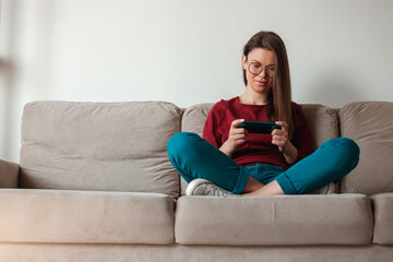 Obraz premium Woman using mobile phone, holding in hands sitting on sofa