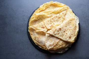 Pancakes, flat and round flour products made from batter by frying in a pan, lie on a black slate plate against a gray background. Pancakes are used as an independent dish and together with fillings.
