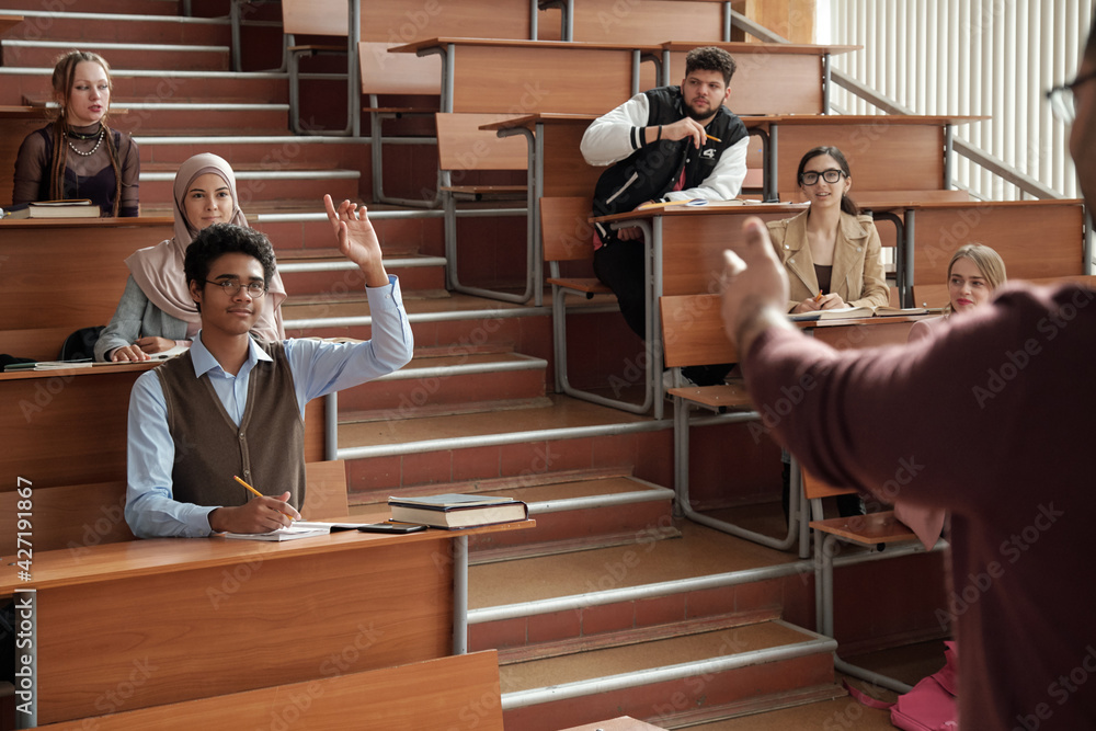Aufkleber young successful student in eyeglasses and casualwear raising hand while sitting by desk on the firs