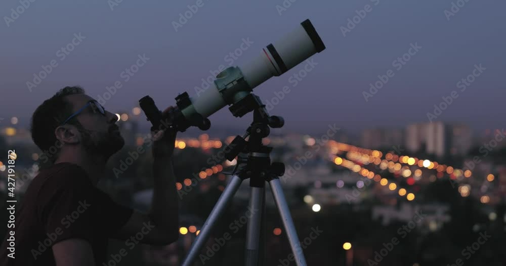 Wall mural amateur astronomer looking at the stars with a telescope with blurred city lights in the background.