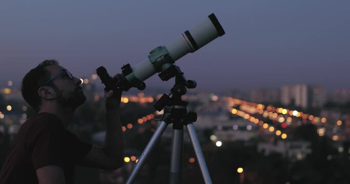 Amateur astronomer looking at the stars with a telescope with blurred city lights in the background.