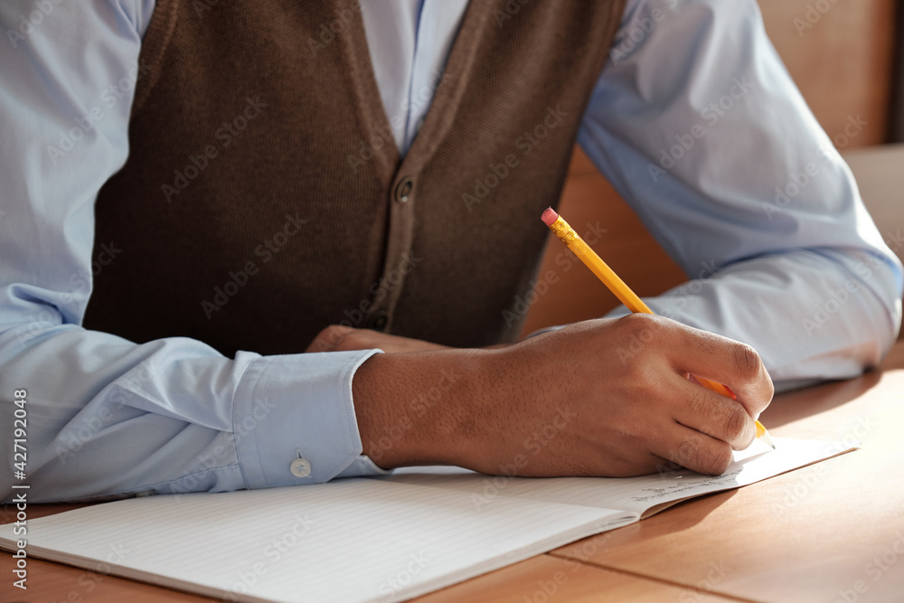Poster Hands of mixed-race guy in smart casualwear bending over desk and making notes or drawing sketch in copybook during lecture
