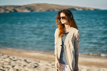 woman on the sand on the beach near the sea in a coat travel tourism sunglasses