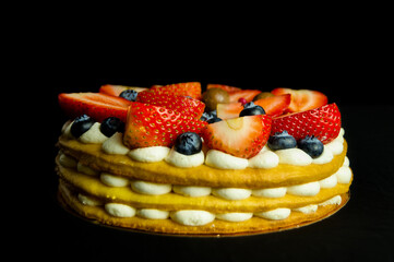 Top view on homemade vanilla birthday cake decorated with berries: strawberries, blueberries, raspberries on black board. Celebration, party cake.