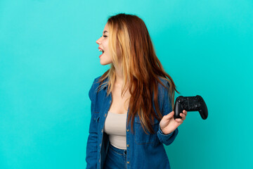 Teenager blonde girl playing with a video game controller over isolated wall laughing in lateral position