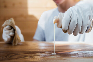 A girl in work gloves pours oil on a wooden tabletop. Coating wood with oil