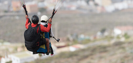 Flying tandem paragliders over the city on a sunny day