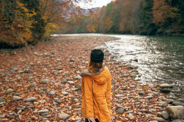 woman in a yellow jacket travels in the autumn forest river mountains