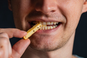 Young man bites fries. Extreme close up. Guy eats eating fried potatoes, isolated. Male mouth.