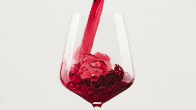 Red wine forms beautiful wave. Close-up shot. Wine pouring in wine glass over balack background. Slow motion of pouring red wine from bottle into goblet