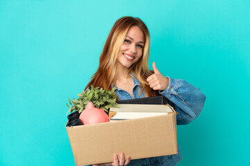 Teenager blonde girl making a move while picking up a box full of things giving a thumbs up gesture