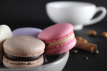 Macaroons on a gray plate at the back stands a cup of coffee or tea coffee beans and cinnamon sticks on a black background with a place for text and with a copyspace