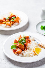 Fried chicken in tomato sauce with rice on white plate, gray background.