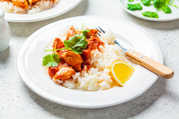 Fried chicken in tomato sauce with rice on white plate, gray background.