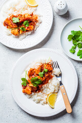 Fried chicken in tomato sauce with rice on white plate, gray background, top view.