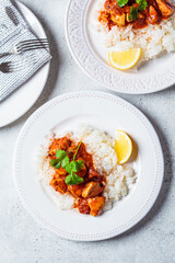 Fried chicken in tomato sauce with rice on white plate, gray background, top view.