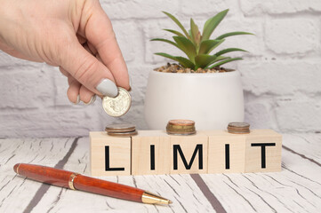 A hand places coins on wooden cubes with the inscription LIMIT, on an office background