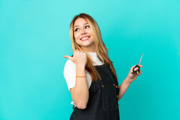 Fototapeta premium Young hairdresser girl over isolated blue background pointing to the side to present a product