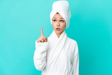 Teenager blonde girl in a bathrobe over isolated blue background thinking an idea pointing the finger up