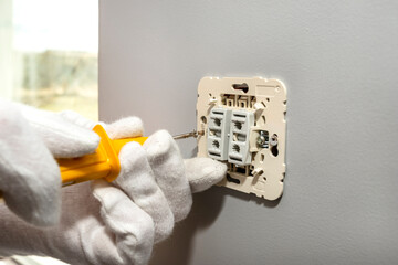 The electrician screws the roller shutters switch up and down with a yellow screwdriver in the room...