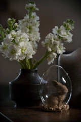 Eastern scene with white flowers in a mini vase and decorative rabbit in a glass egg on the table