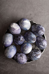 organic Easter eggs close-up, hand-painted with natural blueberries, lie in a clay cup on a stone table. Easter concept. flat lay