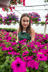 Portrait of young female gardener in apron working with plants in pots in greenhouse