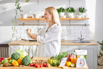 Excited caucasian female have fun in kitchen, with fresh organic vegetarian food on table