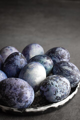 organic Easter eggs on a dark background, hand-painted with natural blueberries, lie in a clay cup on a stone table. Easter concept.