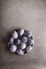 marble Easter eggs on a dark background, hand-painted with natural blueberries, lie in a clay cup on a stone table. Easter preparation concept.