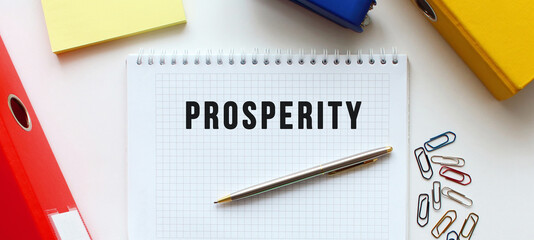 Notepad with text PROSPERITY on a white background, near document folder and office supplies.