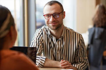 Fototapeta premium Portrait of smiling adult man looking at partner while enjoying business meeting at cafe table, copy space