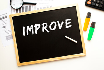 Text IMPROVE written in chalk on a slate board. Office desk with office supplies.