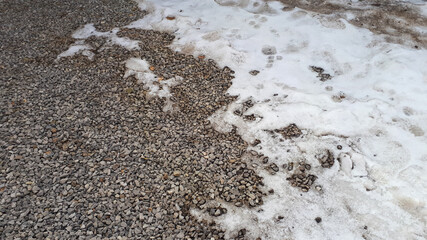 Melting snow on gravel road. Small gravel texture pattern. Rock ground