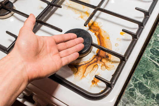 Guy's Hand Points To A Dirty Gas Stove Burner After Home Cooking In The Kitchen