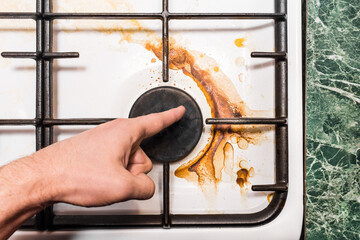 The guy's hand points a finger at the dirty plaque on the gas stove after home cooking in the...