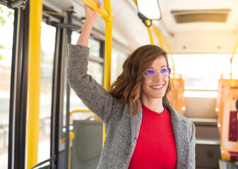 A young woman smiles as she travels standing on a public bus. 