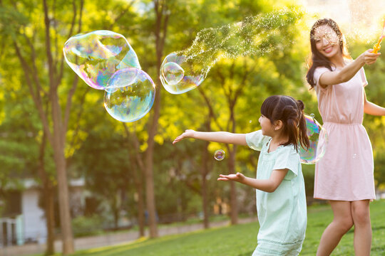 Happy young mother and daughter blowing bubbles on grass