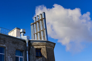 Many chimneys on the roof of an old house smoke against a blue sky
