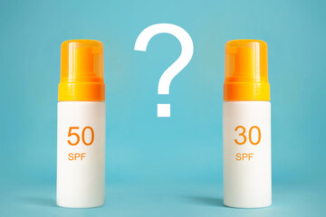 Sunscreen bottles with spf 30 and 50 cream or lotion on the aqua blue background with question. Sun protection, summer skin moisturizer choosing