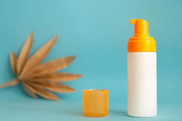 White and yellow sunscreen bottle with cream or lotion on the aqua blue background with palm branch. Empty bottle mockup. Spf sun protection, summer skin moisturizer