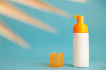 White and yellow sunscreen bottle with cream or lotion on the aqua blue background with palm branch. Empty bottle mockup. Spf sun protection, summer skin care