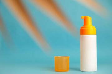 White and yellow sunscreen bottle with cream or lotion on the aqua blue background with palm branch. Empty bottle mockup. Spf sun protection, summer skin care, after sun
